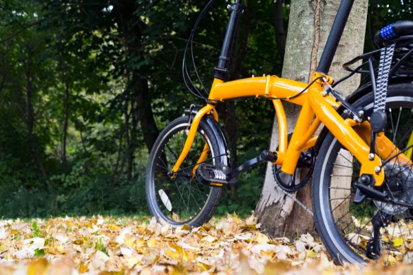Yellow folding bike parked beside a tree on grass in fall.