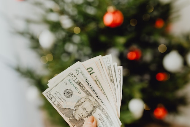 person holding dollars infront of christmas tree..