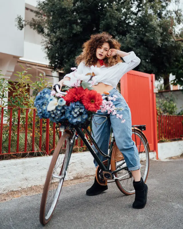 woman posing on her bicycle with flowers in bike basket.
