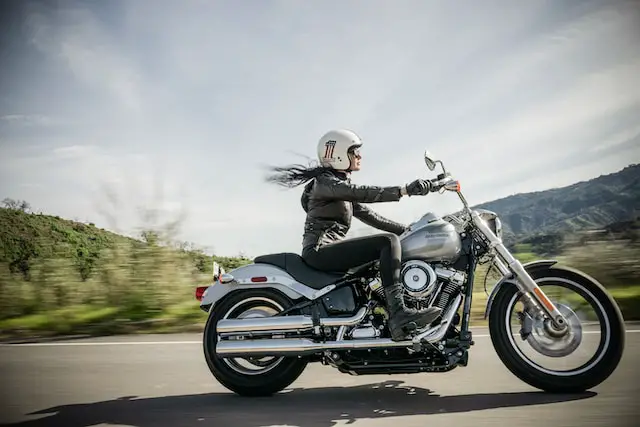 female biker riding a silver harley on road